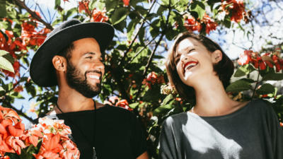 Man and woman smiling at each other in front of a rose bush